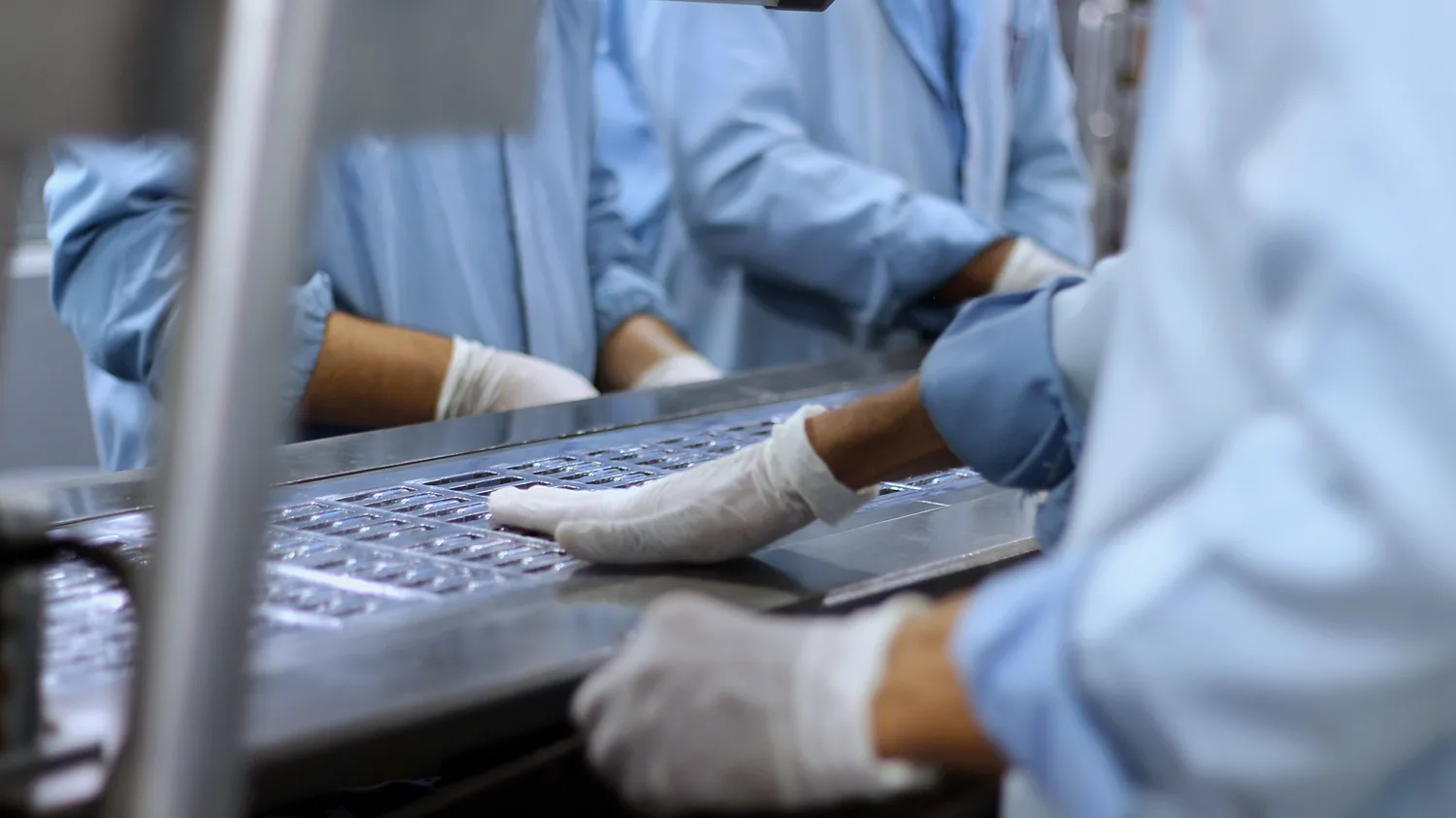 Technicians in cleanroom gowns handling components on a production line in China.